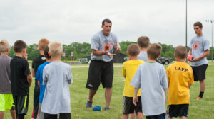 8645: Former Baltimore Ravens  member Sean Considine, center, explains how to receive a handoff from the quarterback during the Sean Considine Football Camp held at Byron High School Sunday, June 8. Considine and several Byron football coaches and players showed 1st through 6th grade students  some of the fundamentals and fun of football.