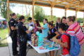 Police officers Lopez and Brox are stationed at a table, surrounded by kids handing out books to anyone who wants one.